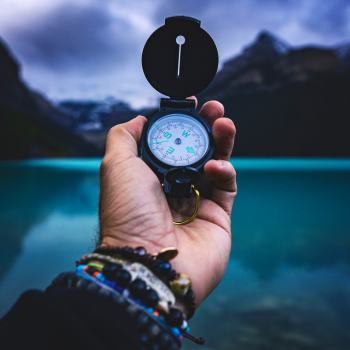 Man holding a compass in front of lake